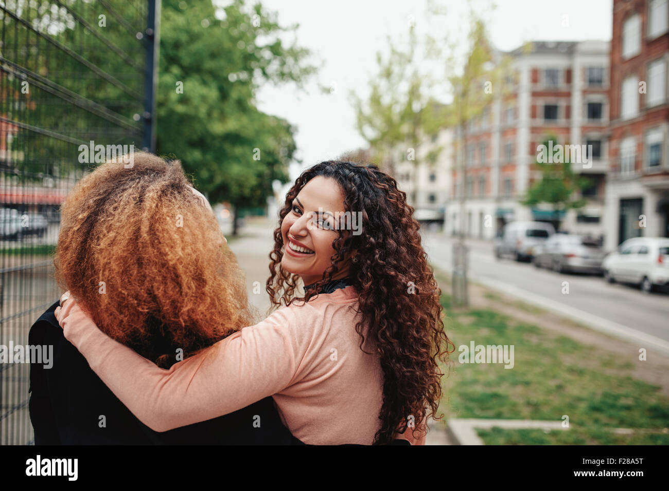 Rear view shot of young woman walking with her friend looking back over her shoulder. Two women walking along city street. Stock Photo