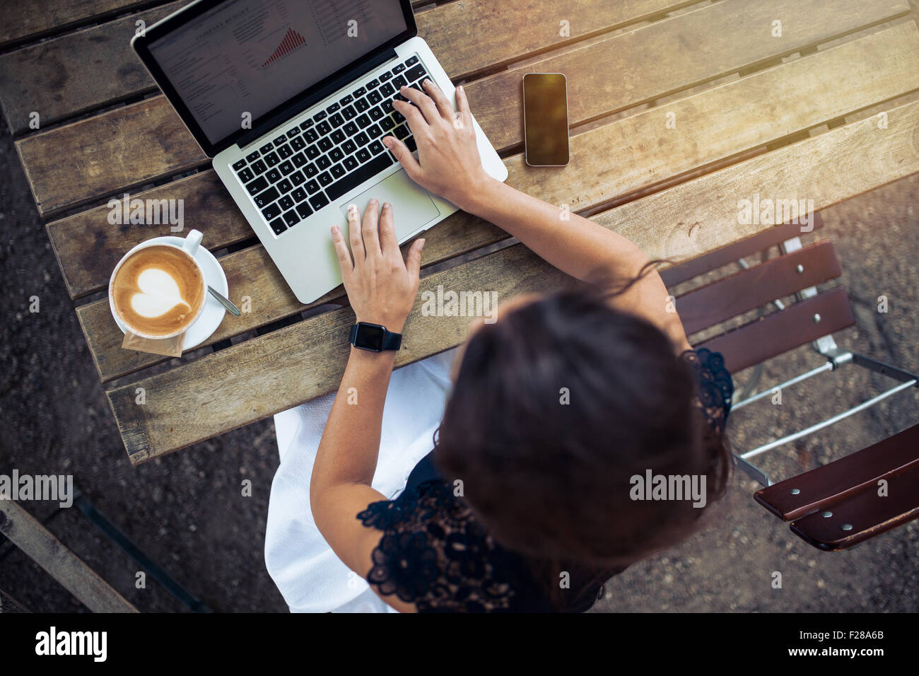 Top view of female using her laptop at a cafe. Overhead shot of young woman sitting at a table with a cup of coffee and mobile p Stock Photo