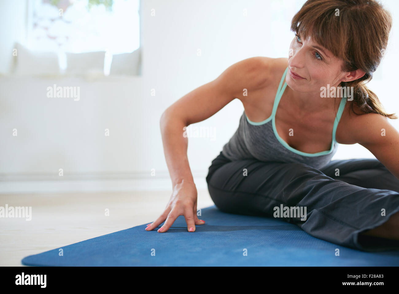 Image of woman bending forward doing yoga . Fitness woman practicing yoga on exercise mat at gym looking away. Stock Photo