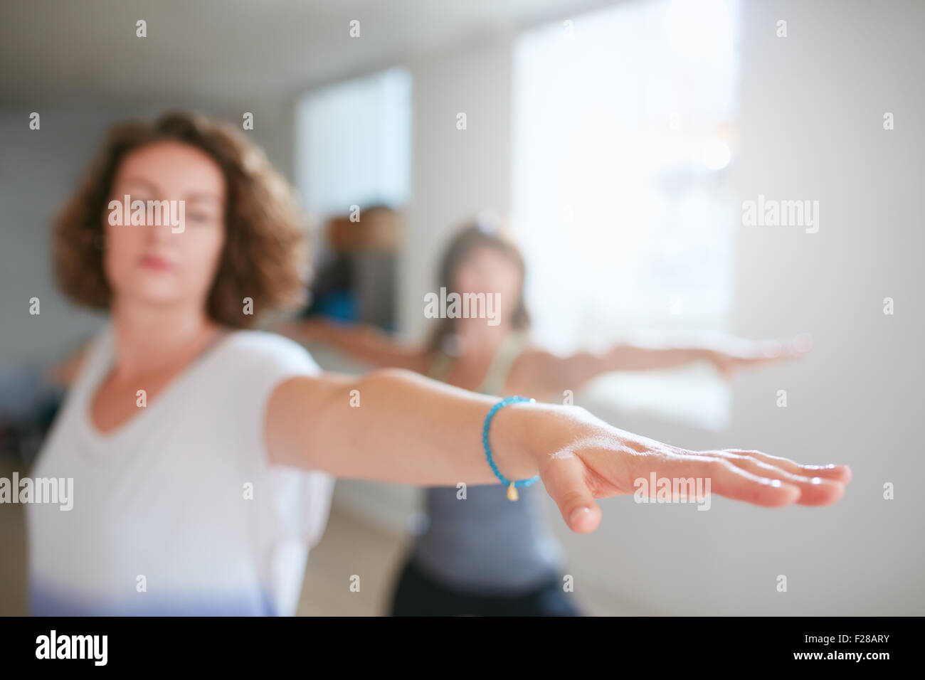 Fitness woman stretching her arms at yoga class. Young woman performing yoga in warrior pose. Virabhadrasana. Focus on hand. Stock Photo