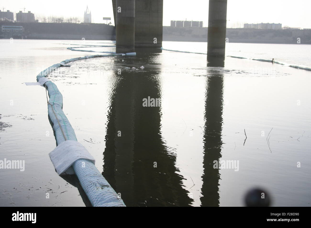 A temporary barrier with oil-absorbing materials is placed to control diesel oil leaking from a pipeline on the Yellow River in Stock Photo