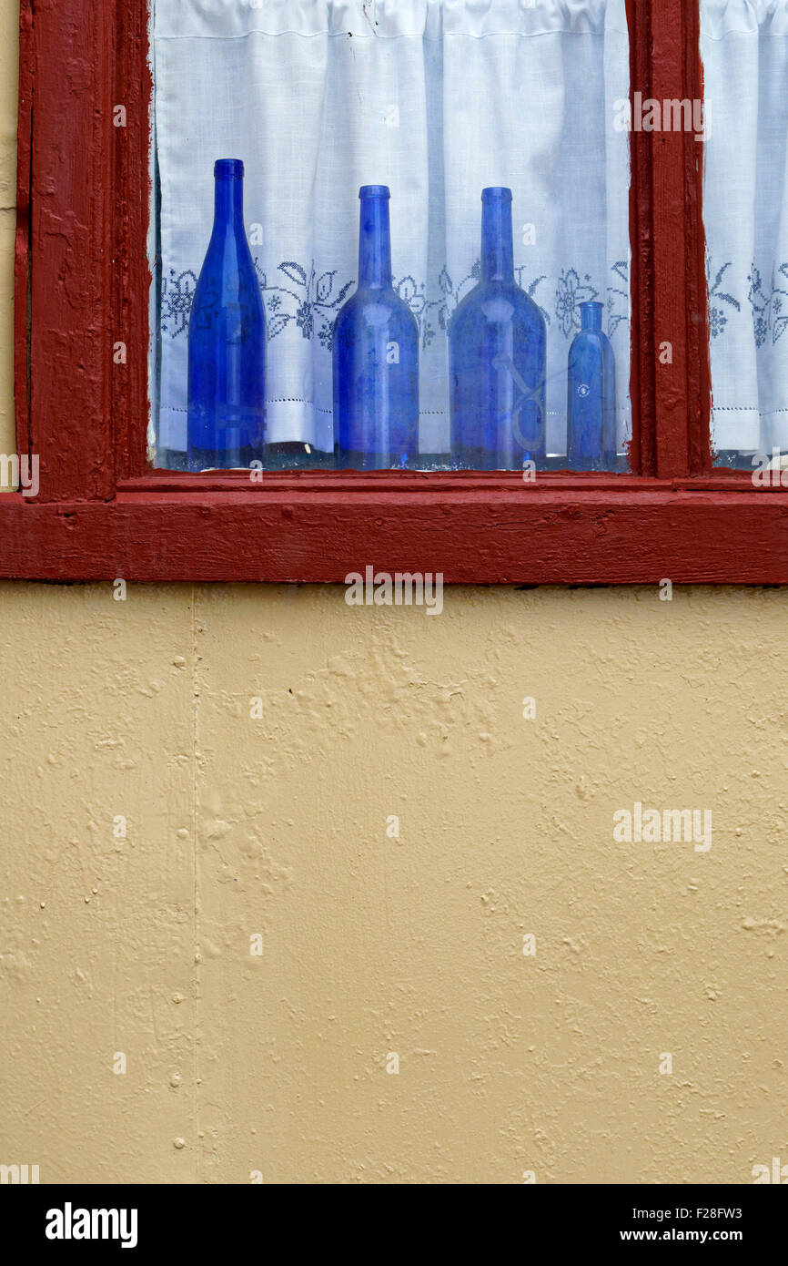 4 Blue bottles standing in red framed window, Flatey, Iceland Stock Photo