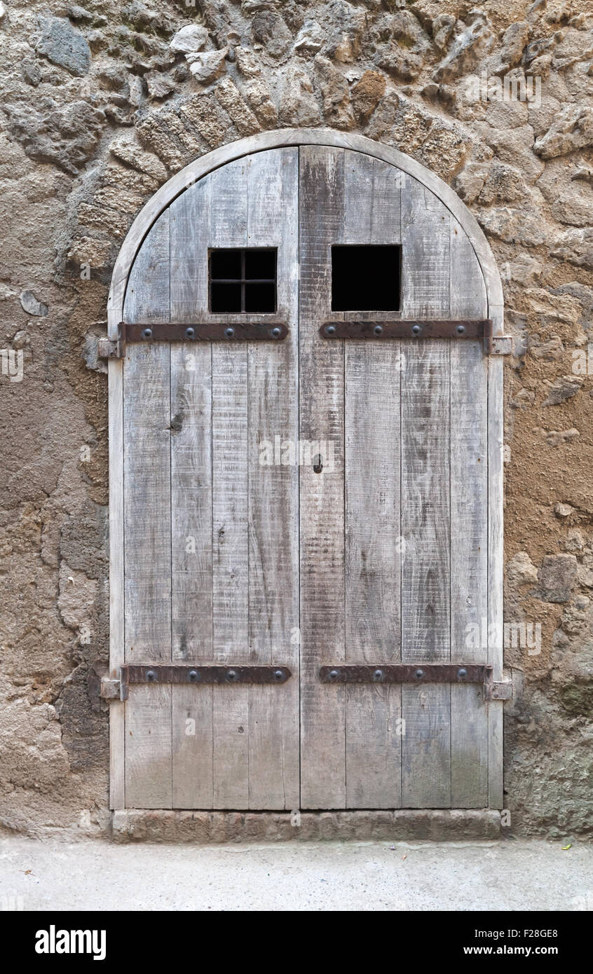 Old wooden door with arch in old stone wall, background texture Stock Photo