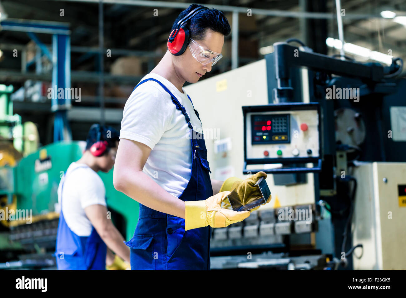 Asian machine operator in production plant checking data Stock Photo