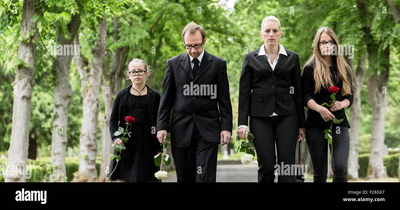 Family on cemetery walking down alley at graveyard with roses Stock Photo