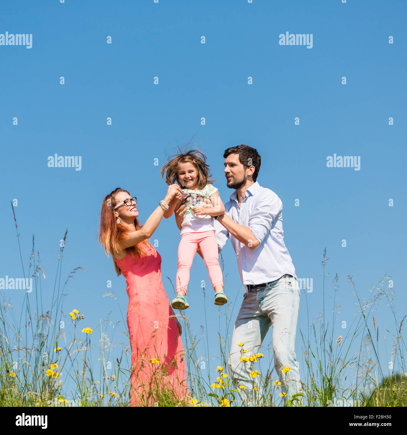 Family of mother, father and child on meadow, dad carrying the daughter Stock Photo