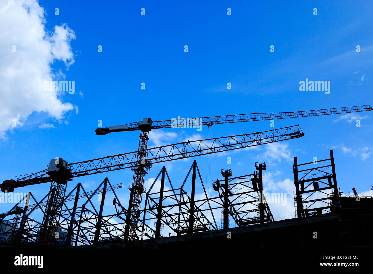 Cranes on construction site silhouette against blue sky. Stock Photo