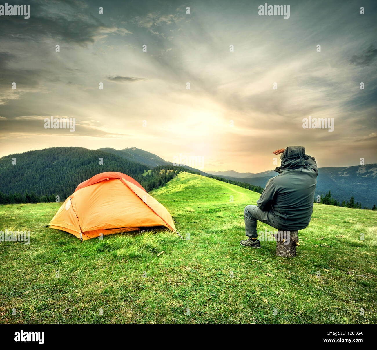 Man sitting near tent looking at the setting sun over mountains Stock Photo