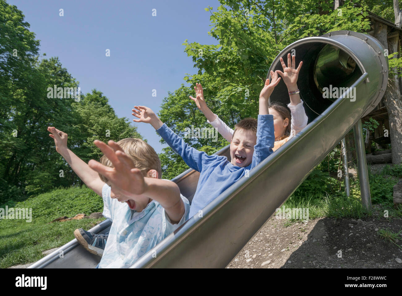 Three friends sliding down on slide in playground, Munich, Bavaria, Germany Stock Photo