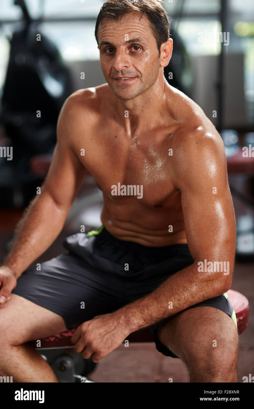 Athletic shirtless sweaty man sitting on a bench in the gym, resting after  workout Stock Photo - Alamy