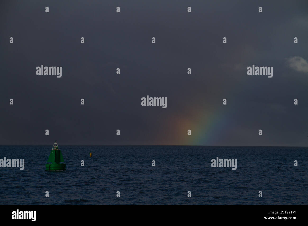Rainbow above a dark sea with a green buoy Stock Photo - Alamy