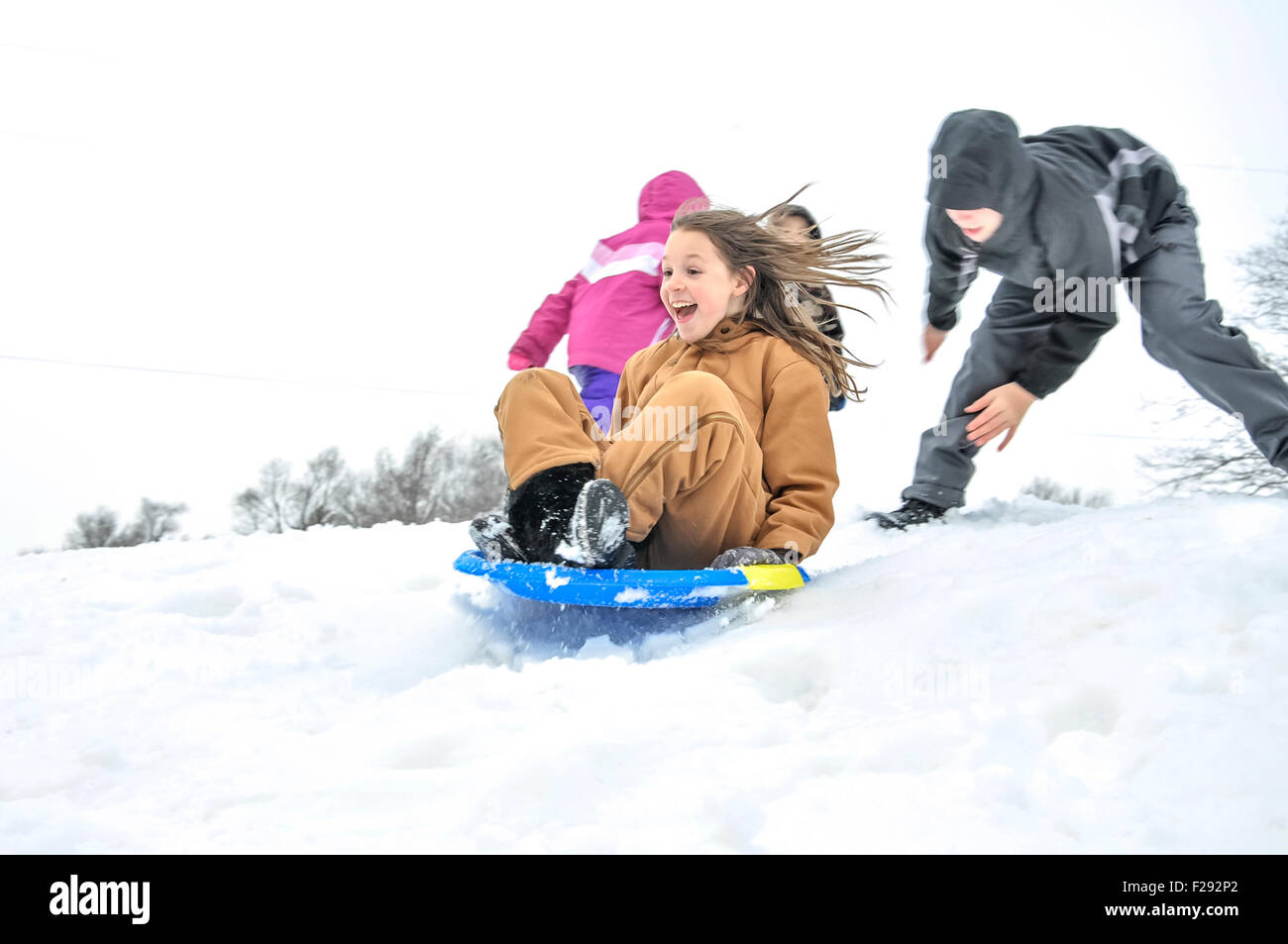 Girl gets pushed down snowy hill in sled Stock Photo