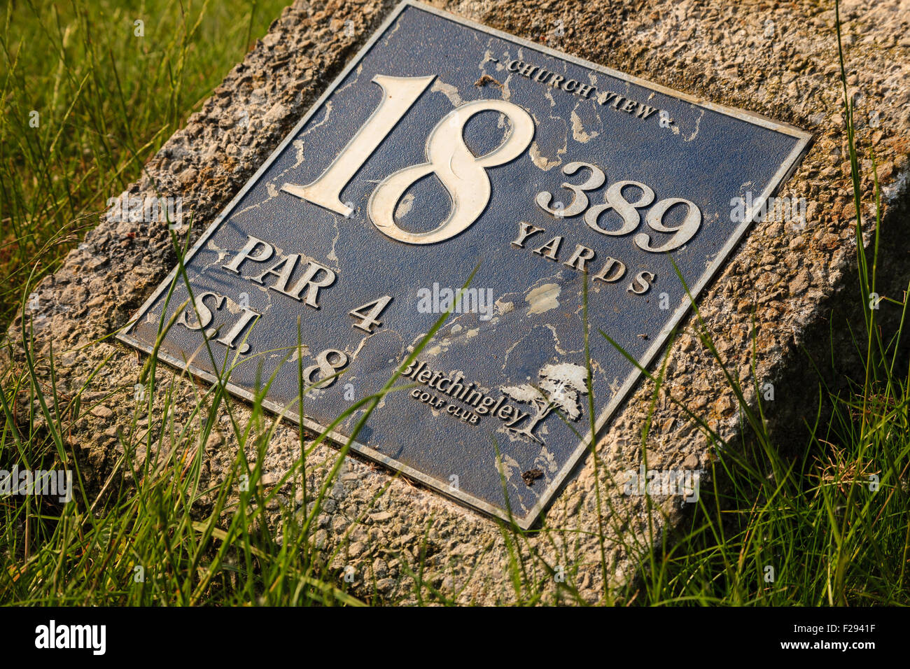A hole and distance marker sign plaque set into concrete on a golf