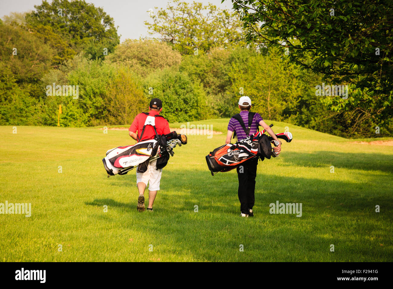 Two men carrying golf bags walk away across the course on a sunny, late spring afternoon in the