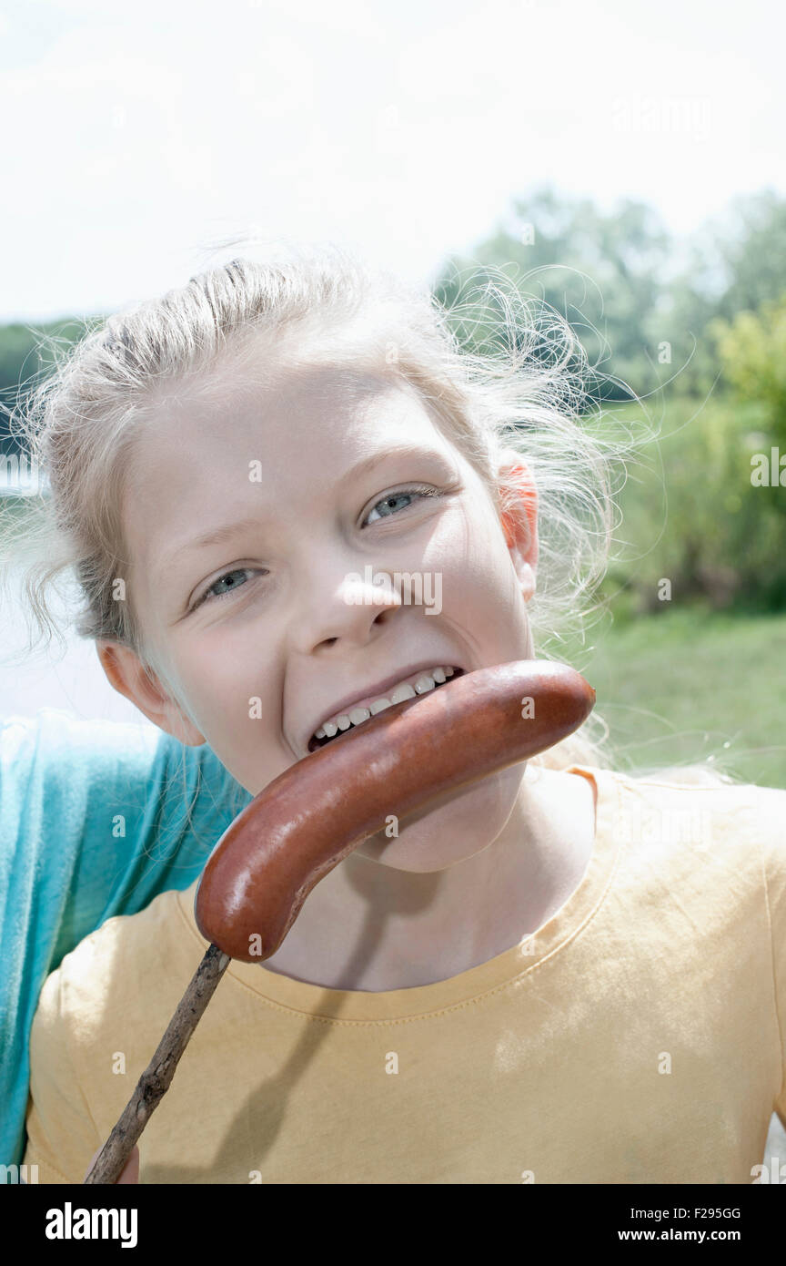 Girl eating a roasted sausage at lakeside, Bavaria, Germany Stock Photo