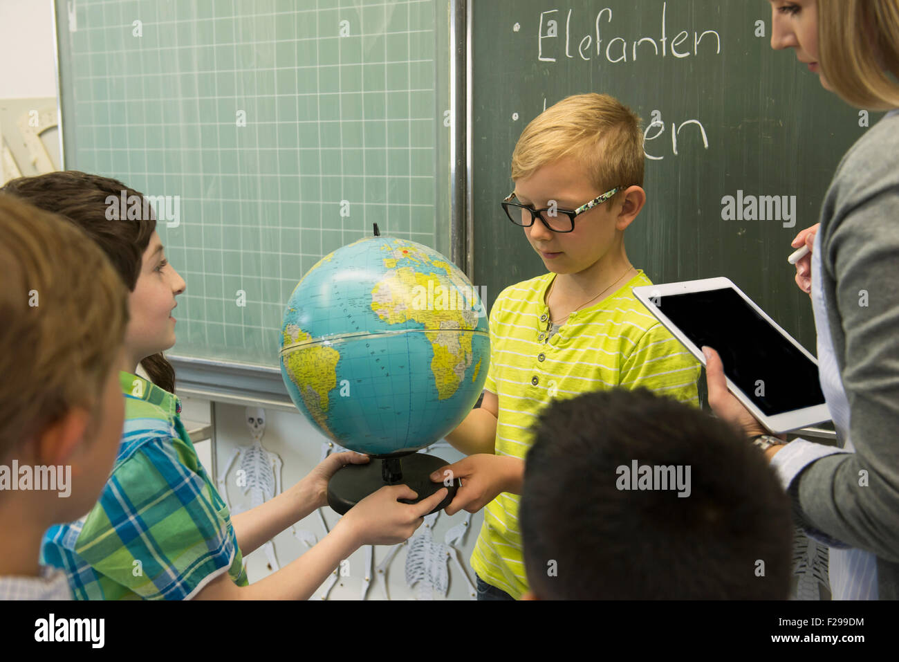 Female teacher and students looking at globe in classroom, Munich, Bavaria, Germany Stock Photo