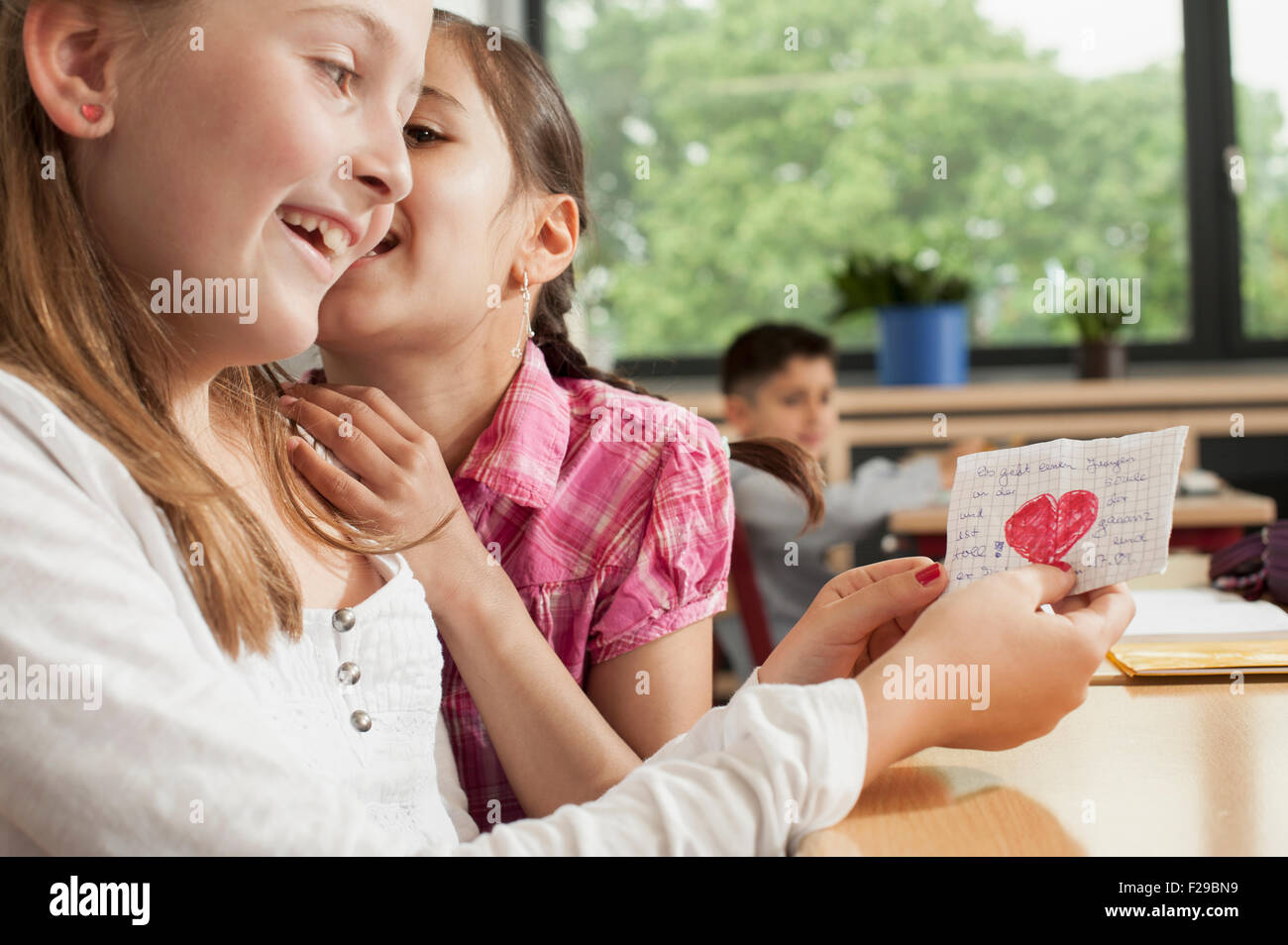 schoolgirls whispering in classroom and showing a love letter, Munich, Bavaria, Germany Stock Photo