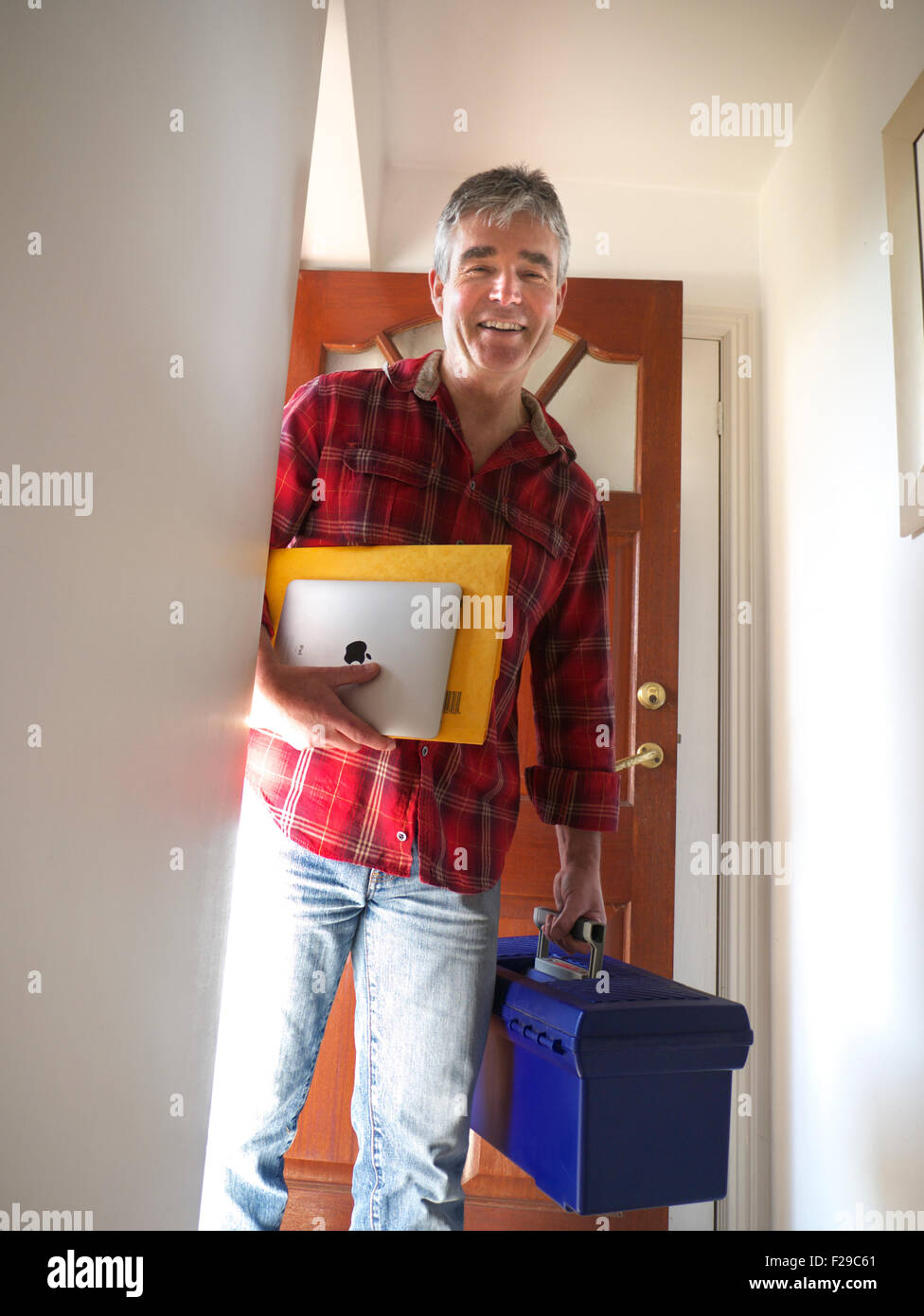 DOMESTIC WORKMAN IPAD TECHNICIAN Happy smiling tradesman with iPad arriving at open door of domestic home for security repair boiler maintenance work Stock Photo