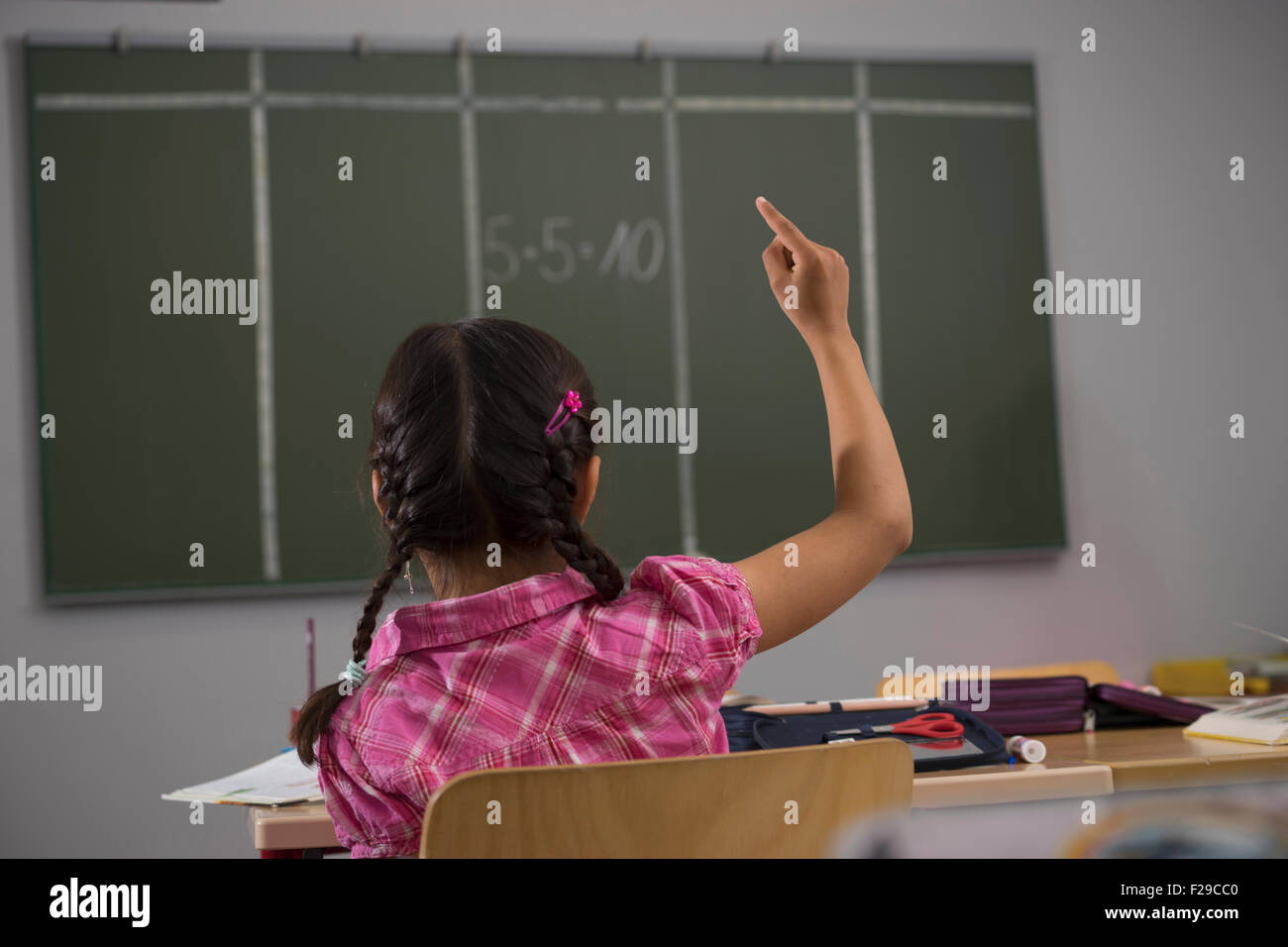 schoolgirl in front of blackboard with raised hand in classroom, Munich, Bavaria, Germany Stock Photo