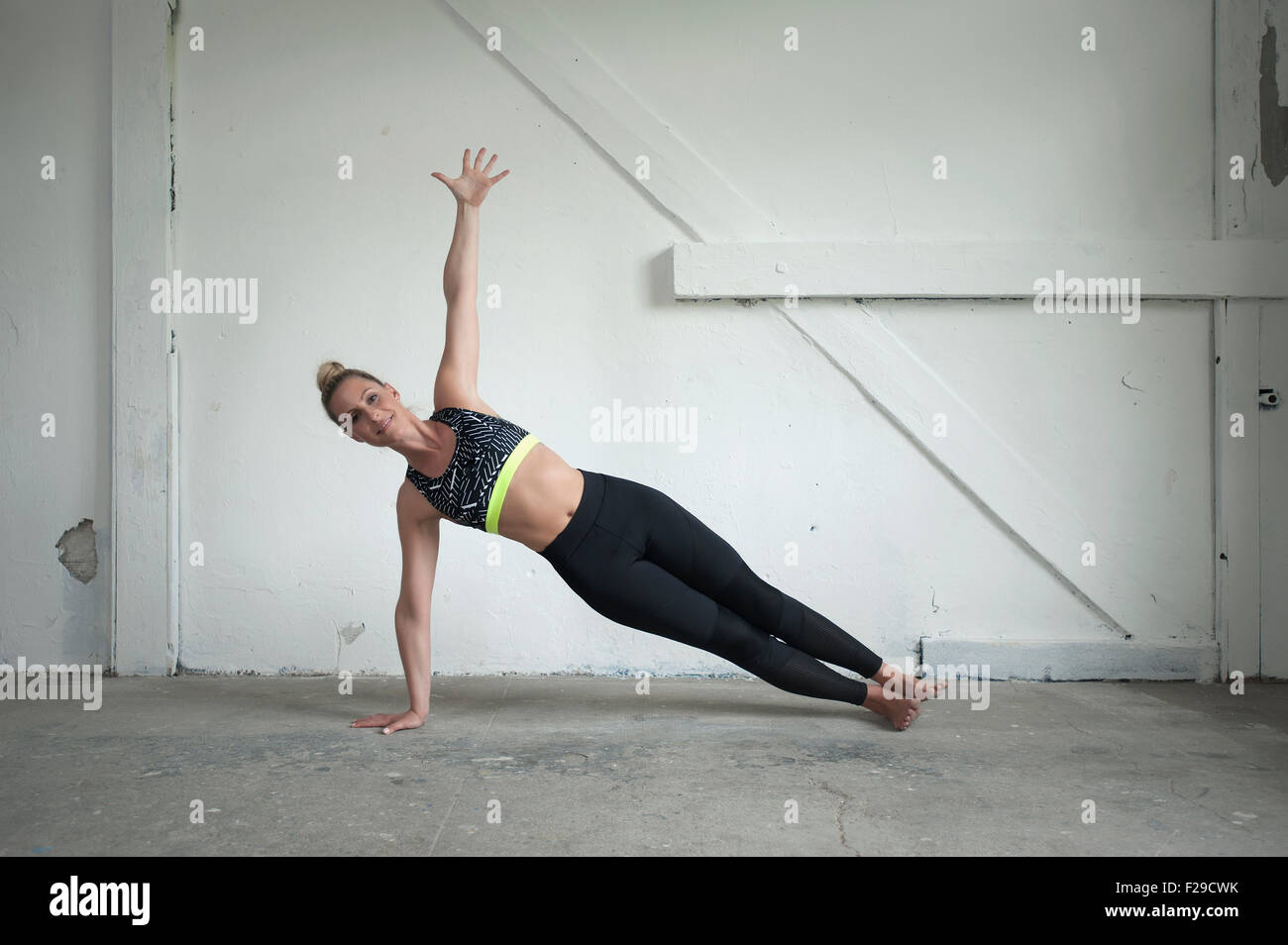 Mid adult woman practicing side plank pose in yoga studio, Munich, Bavaria, Germany Stock Photo