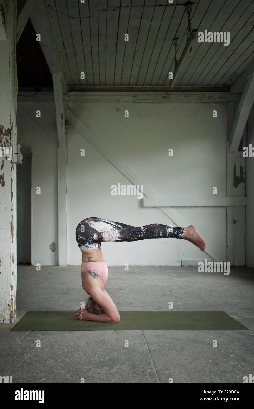 Mid adult woman practicing headstand pose in yoga studio, Munich, Bavaria, Germany Stock Photo