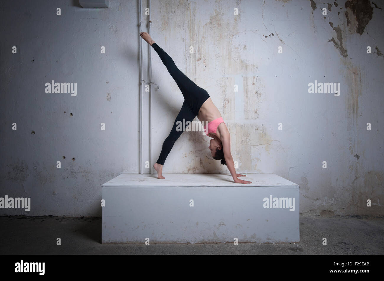 Mid adult woman practicing one legged downward facing dog position on concrete block, Munich, Bavaria, Germany Stock Photo