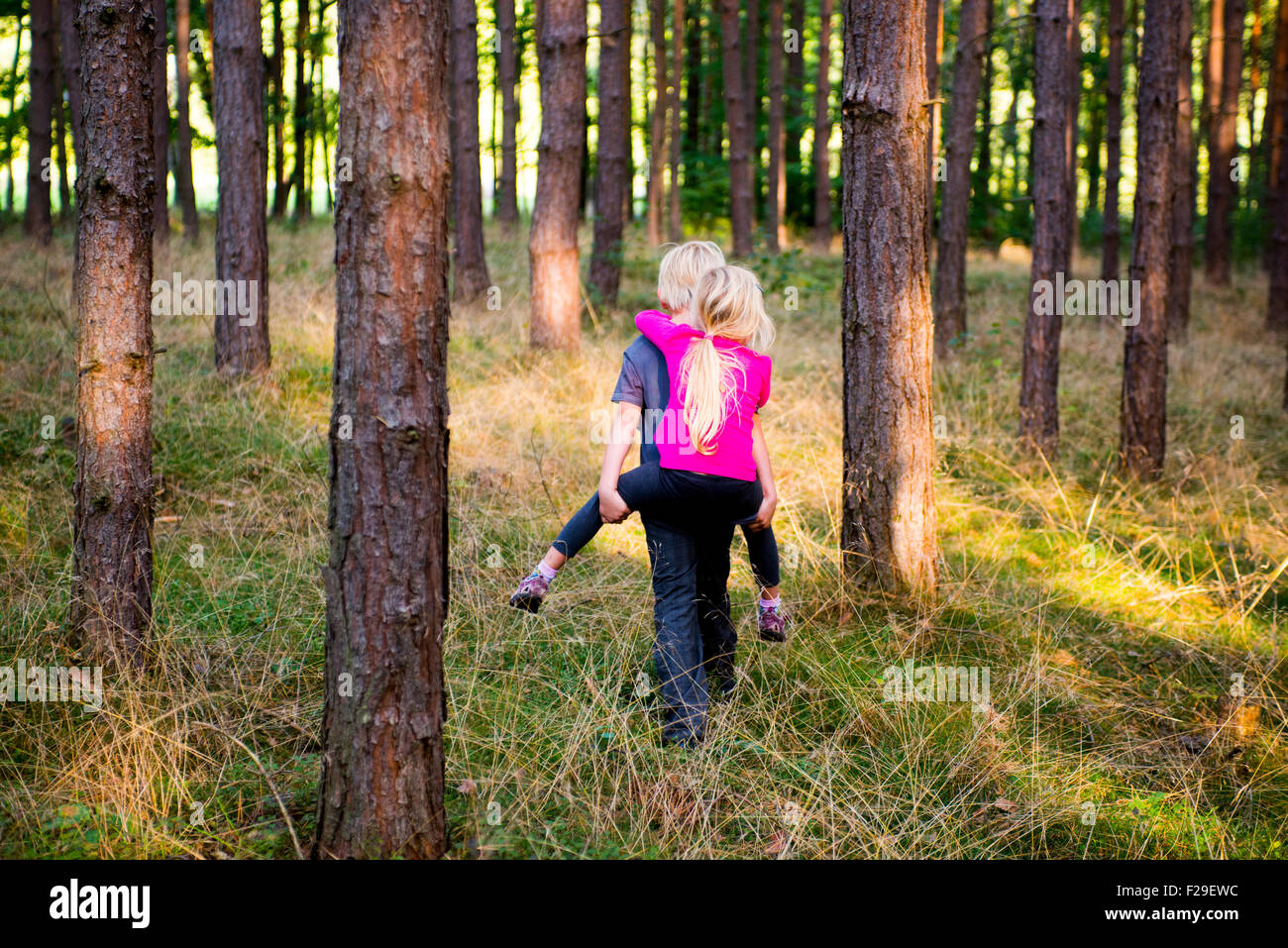 Young boy giving young girl piggyback outdoors smiling, forest, woodland, wood, summer, holiday, siblings, children playing, kid Stock Photo
