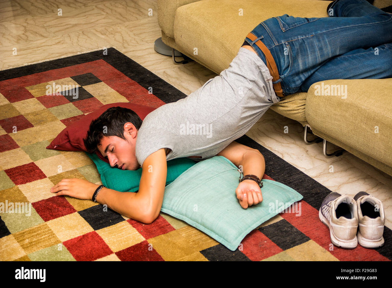 Drunk Young Handsome Man Resting on Couch in the Living Room with Head on the Floor. Stock Photo
