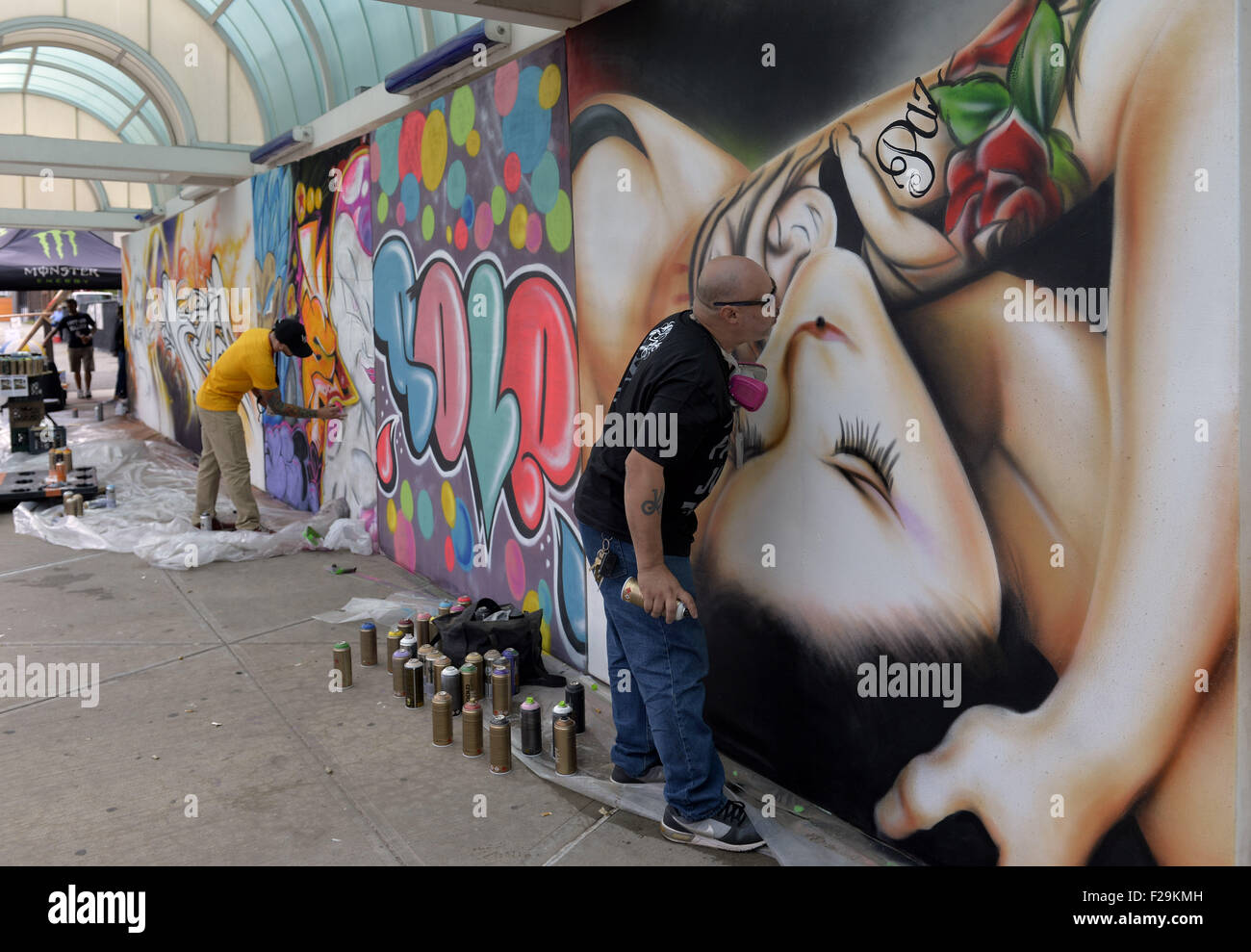 Garden City, New York, USA. 13th Sep, 2015. At right, JAMES SEXER RODRIGUEZ, street name SEXER1, from Bronx, NY, spray paints a mural of a woman, on the wall of urban art paintings by contemporary artists, outdoors at the United Ink Flight 915 Tattoo convention at the Cradle of Aviation Museum in Long Island. The word Paz, peace, is part of the woman's arm tattoo. © Ann Parry/ZUMA Wire/Alamy Live News Stock Photo