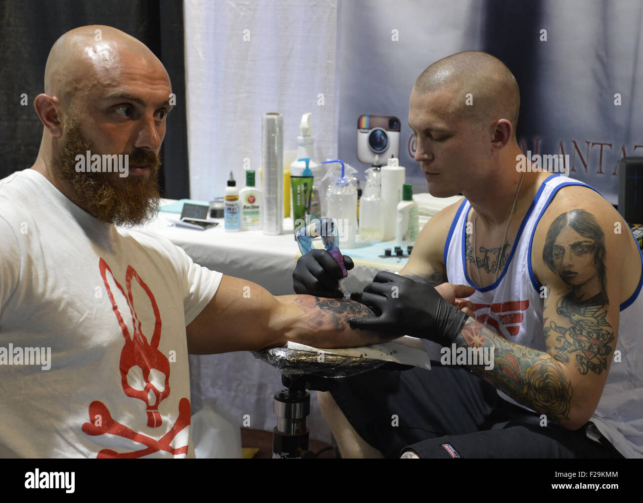 Garden City, New York, USA. 13th Sep, 2015. LUKE PALAN, a tattoo artist from Vegas, is tattooing a man's arm at the United Ink Flight 915 Tattoo convention at the Cradle of Aviation Museum in Long Island. The bearded man is wearing a Psycho Bunny white and red T-shirt. © Ann Parry/ZUMA Wire/Alamy Live News Stock Photo