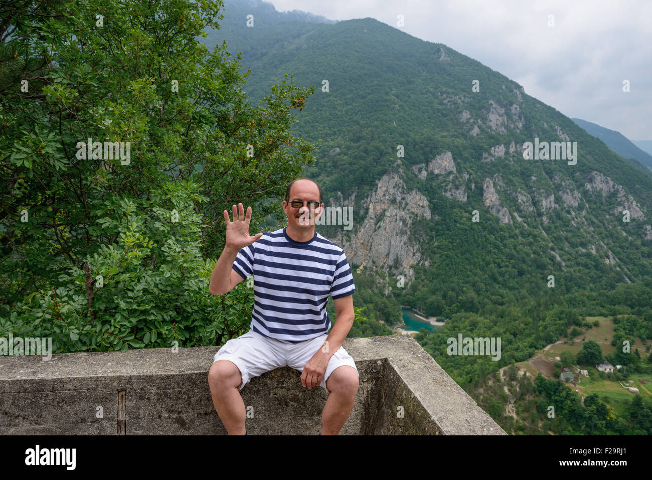 Portrait of mature man that is sitting with greeting gesture at viewing point near actor Bulatovic-Dzambas monument above Devil’ Stock Photo