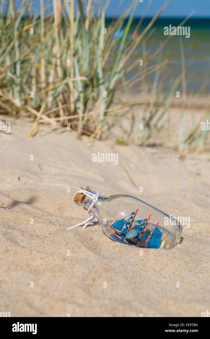 Small ship in the glass bottle lying on the beach, souvenir concept Stock Photo