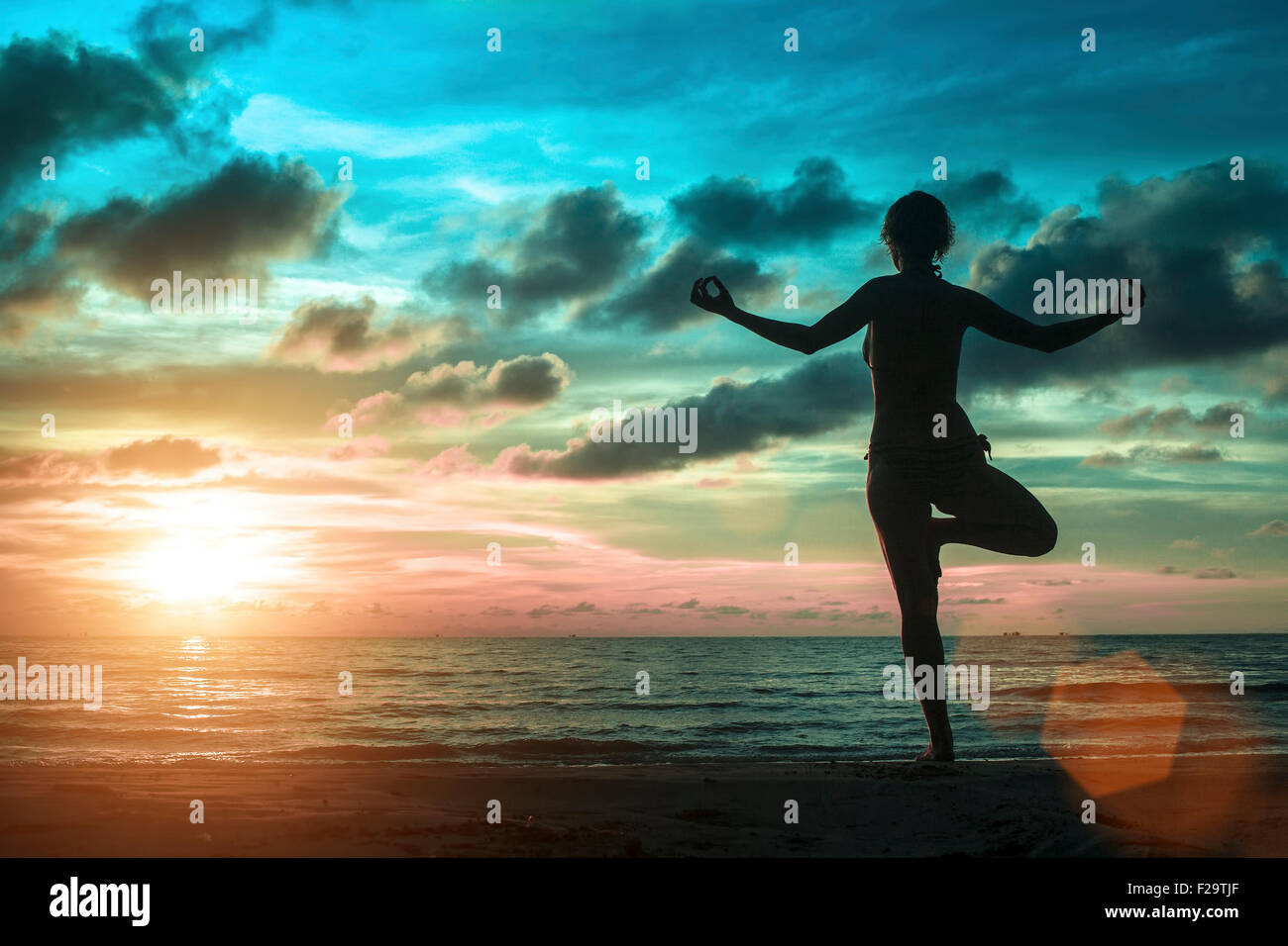 Silhouette of young women standing at yoga pose on the beach during an ...