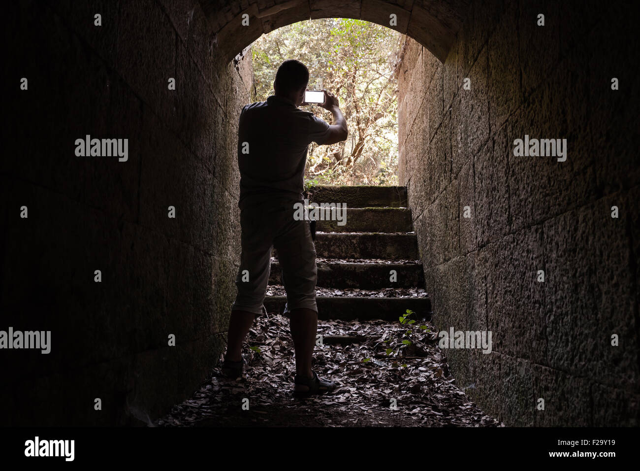 Young man is taking photo on his smartphone from dark stone tunnel Stock Photo