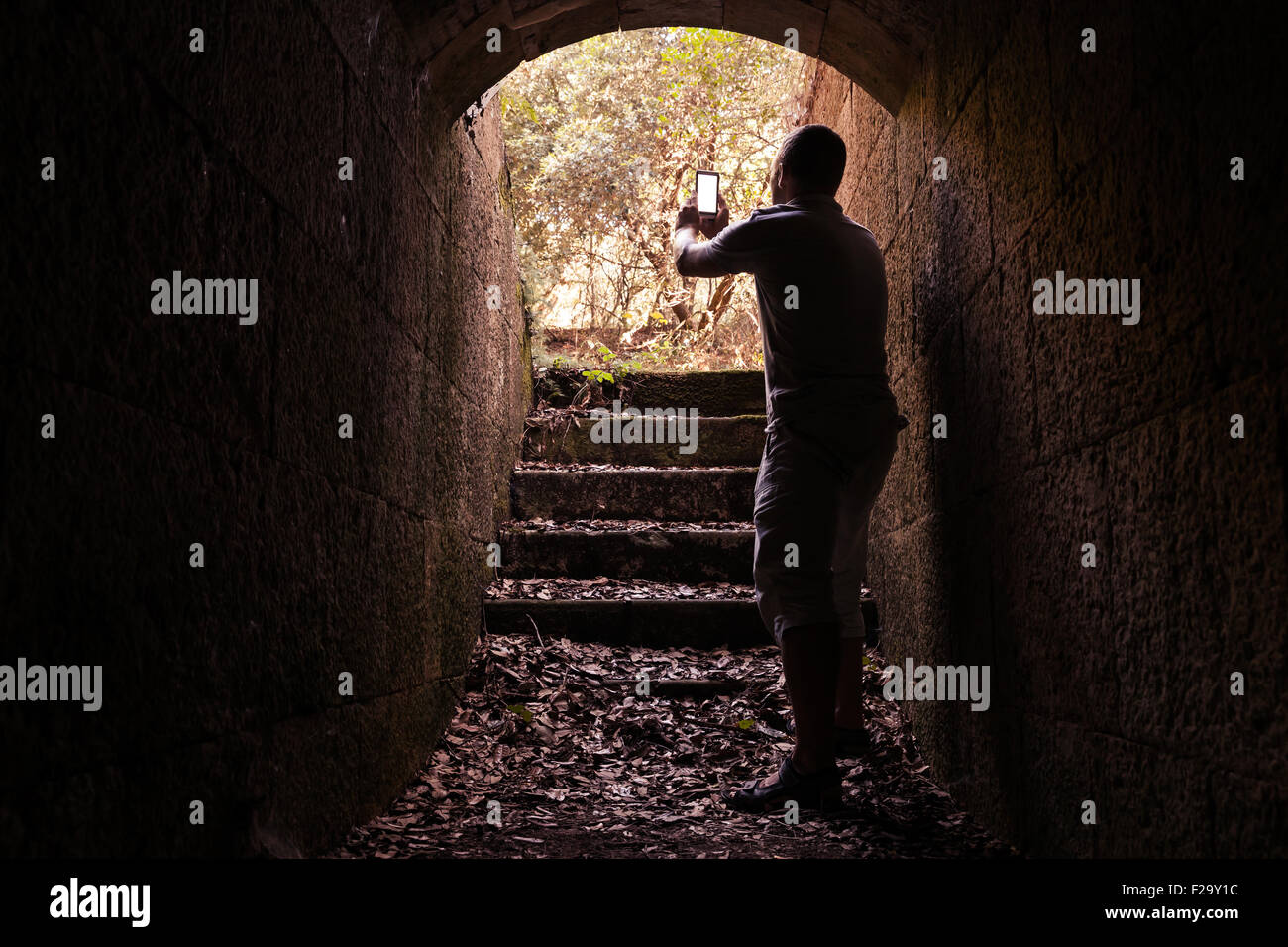 Young man is taking photo on his smart-phone from dark stone tunnel Stock Photo
