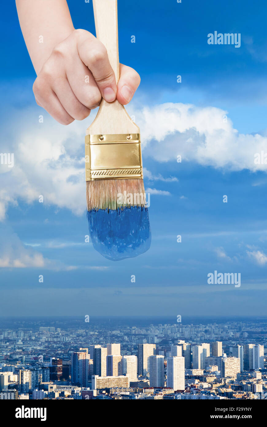 nature concept - hand with paintbrush colors blue sky over blue city Stock Photo