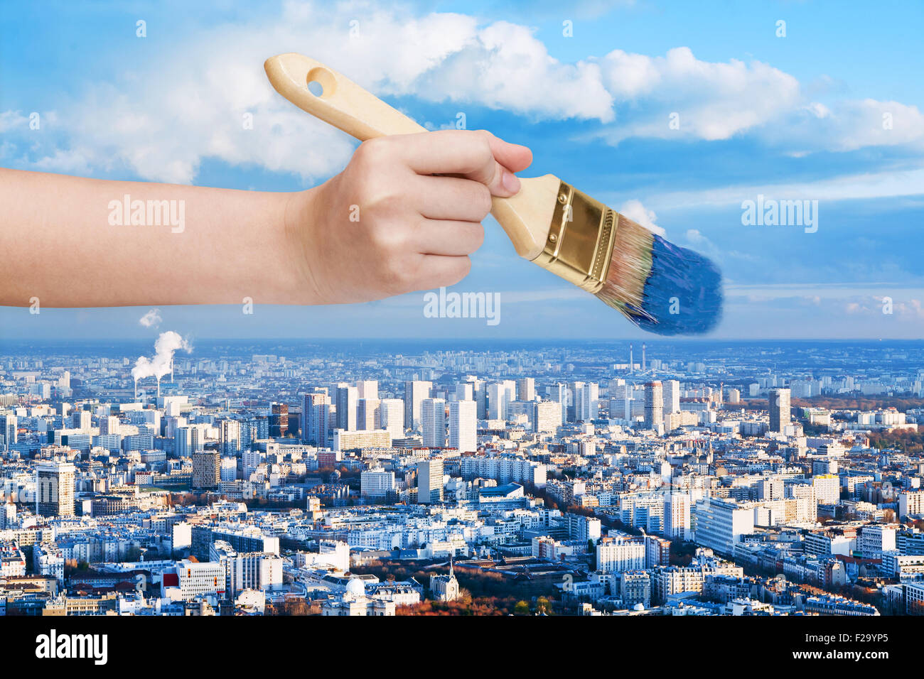 nature concept - hand with paintbrush paints blue sky over big city Stock Photo
