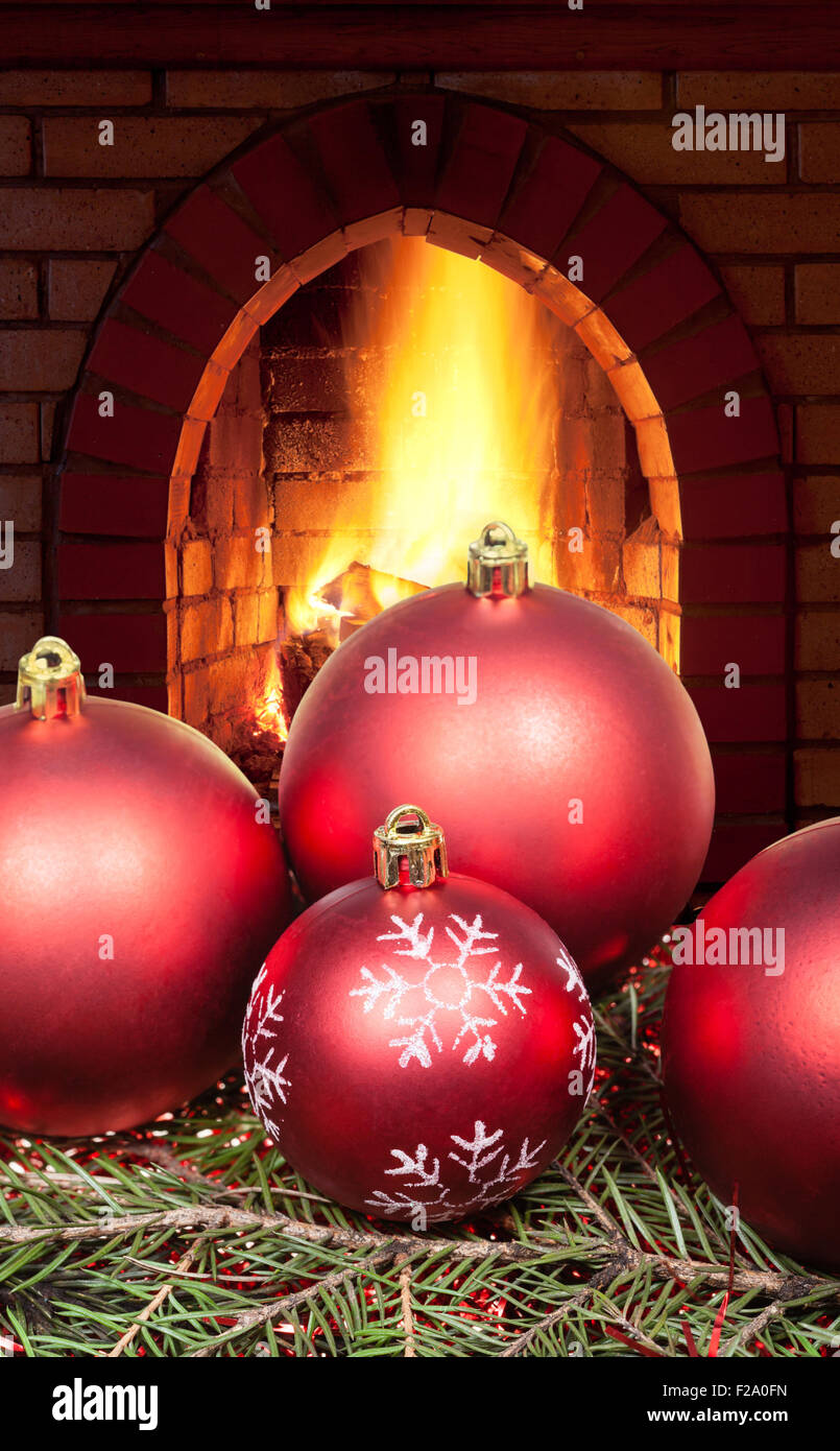 red Christmas balls on green spruce tree with open fire in home fireplace Stock Photo