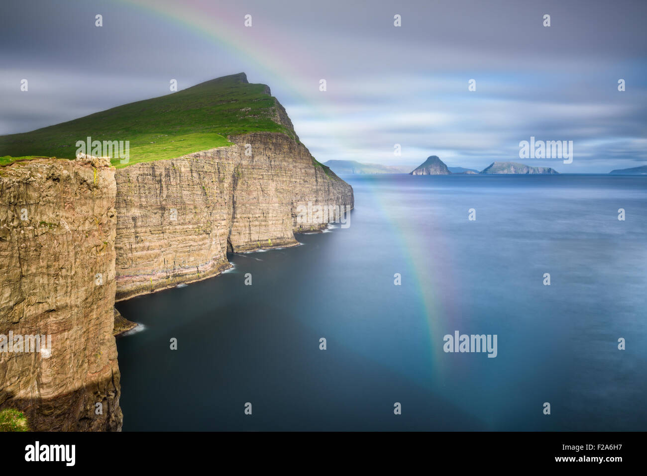 Giant sea cliffs shortly after storm on Faroe Islands with a rainbow. Long exposure. Stock Photo