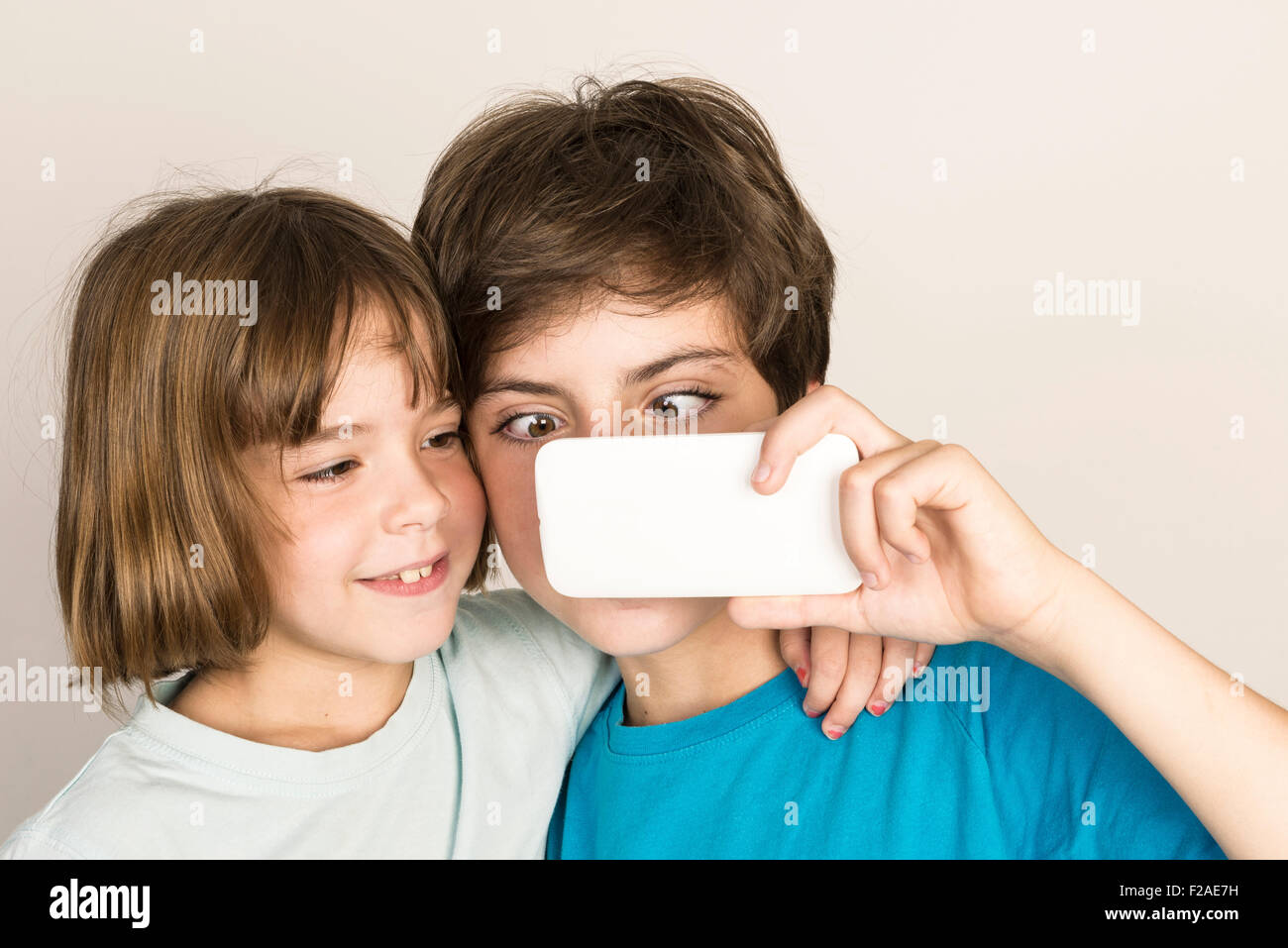 Happy child doing a squint and taking a selfie with a smart phone at home isolated on white background Stock Photo