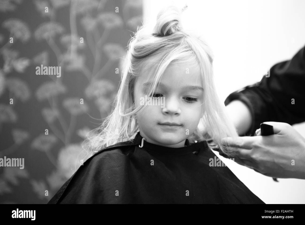 Female hairdresser cutting and brushing young child blond girl hair in hairdressing salon Stock Photo