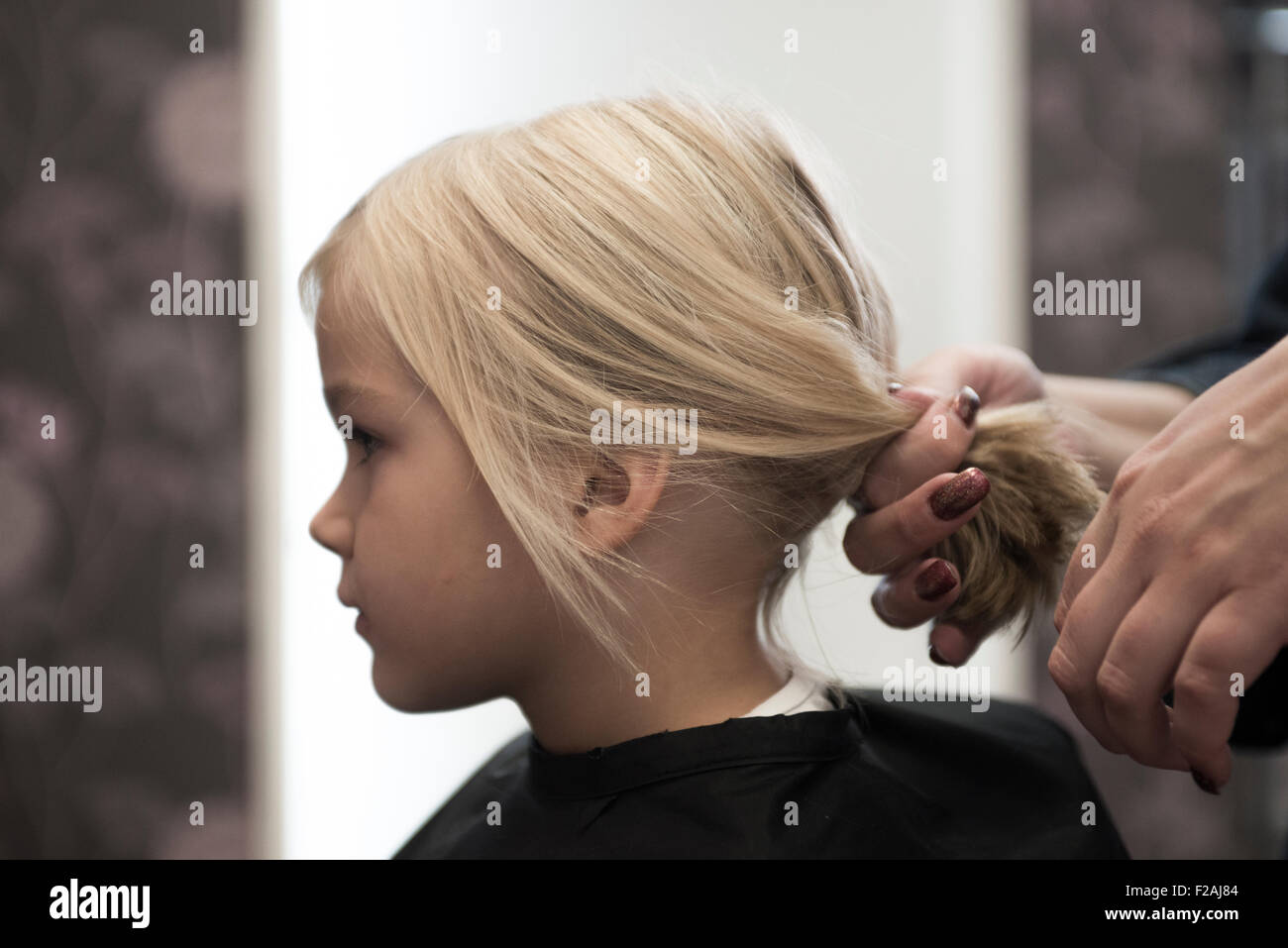 Female hairdresser cutting and brushing young child blond girl hair in hairdressing salon Stock Photo