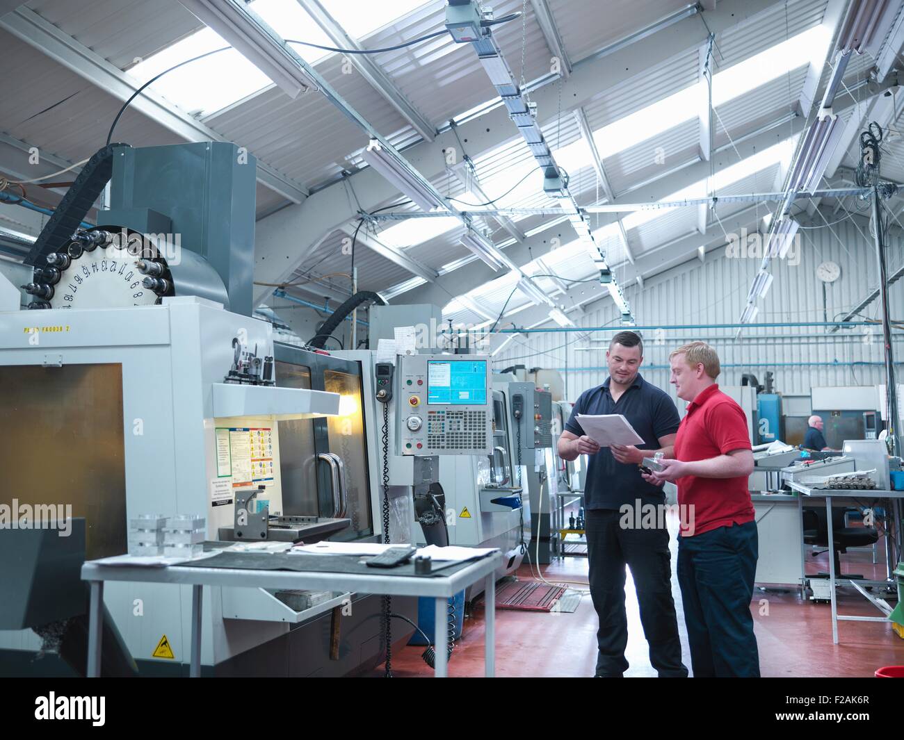 Engineers discussing work in front of CNC machines in engineering factory Stock Photo
