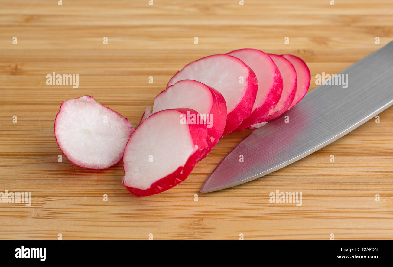 Fresh chopped radishes and a knife on a cutting board on a wooden