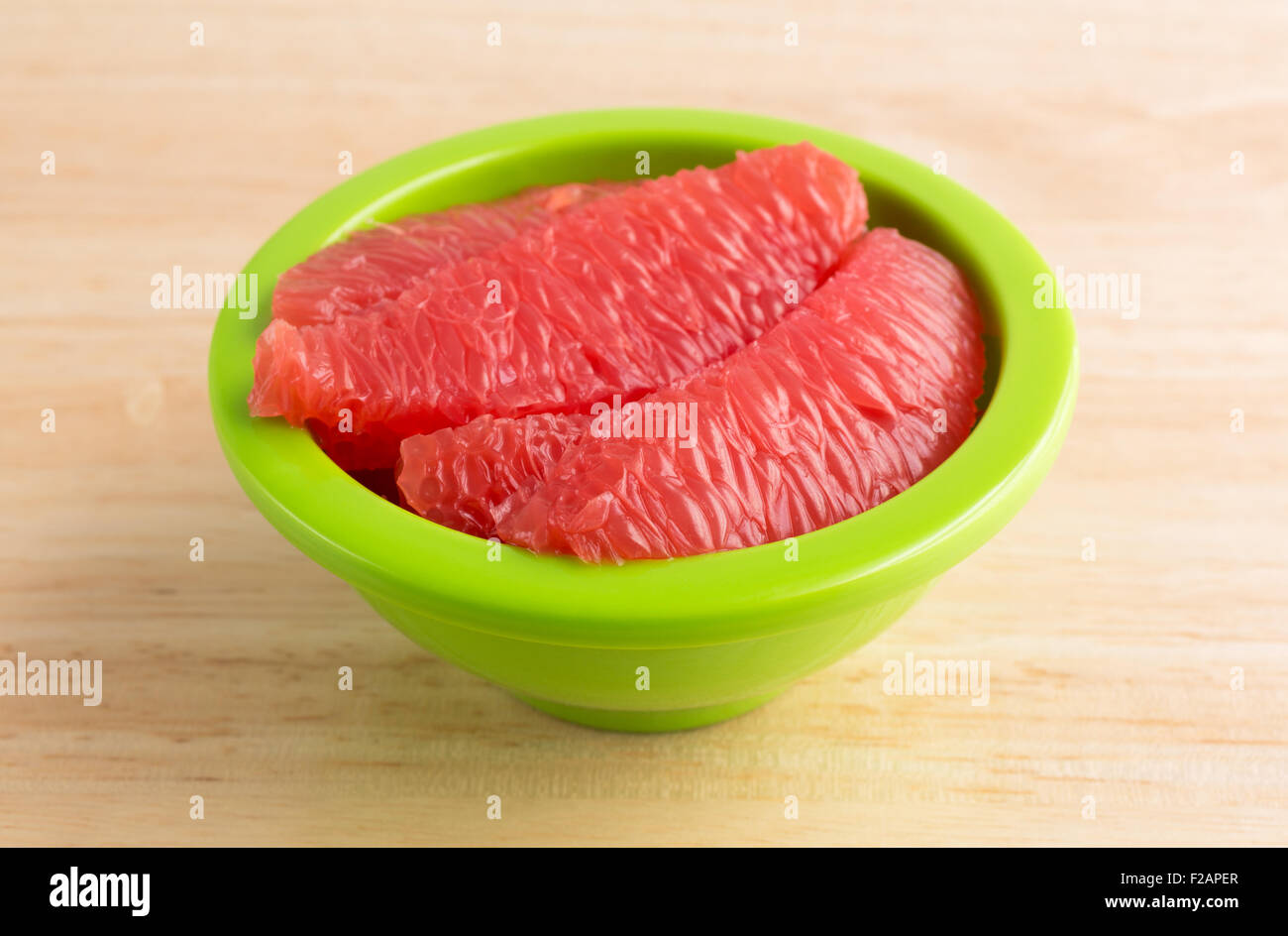 Sections of red grapefruit in a green bowl on a wood table top. Stock Photo