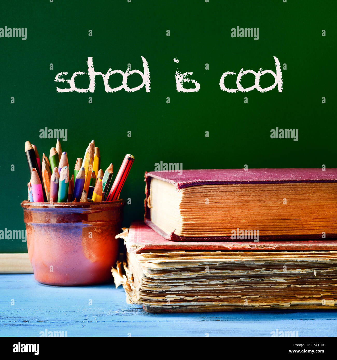 some pencils in a pot, some books on a blue school desk, and the text school is cool written with chalk in a chalkboard Stock Photo