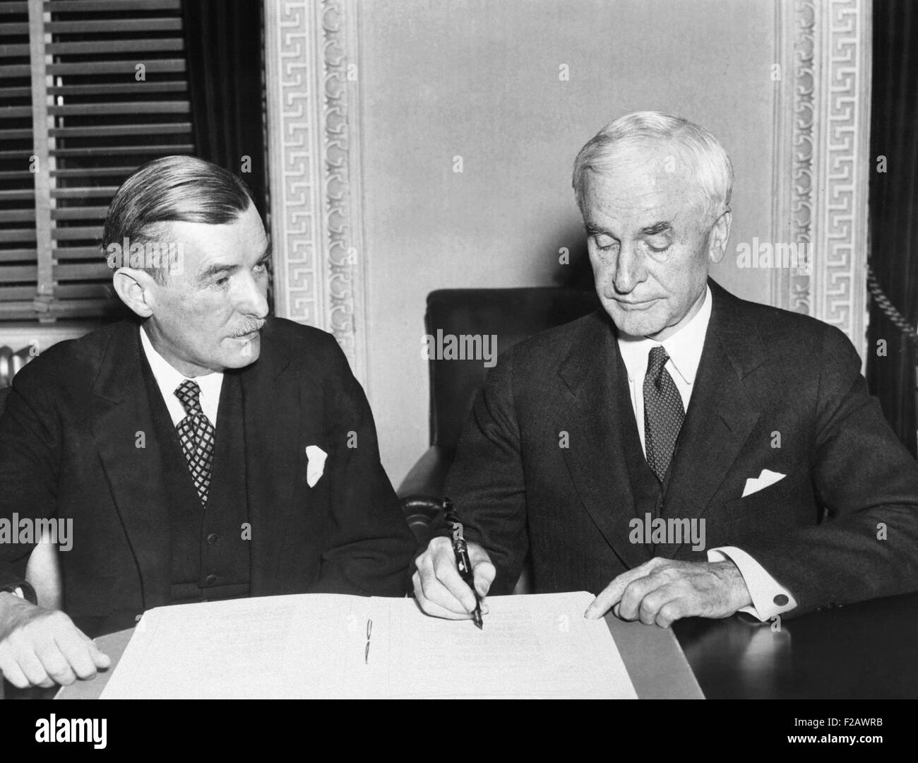 Sec. of State Cordell Hull signs a trade pact between the United States and Czechoslovakia. March 7, 1938. Czechoslovakia Ambassador, Vladimir Hurban, watches as his country became the 17th nation granted preferential trade under the Reciprocal Tariff Act 1934. The pact encouraged US agricultural product exports to Czechoslovakia and Czech imports of manufactured products, particularly shoes. (CSU 2015 11 1226) Stock Photo