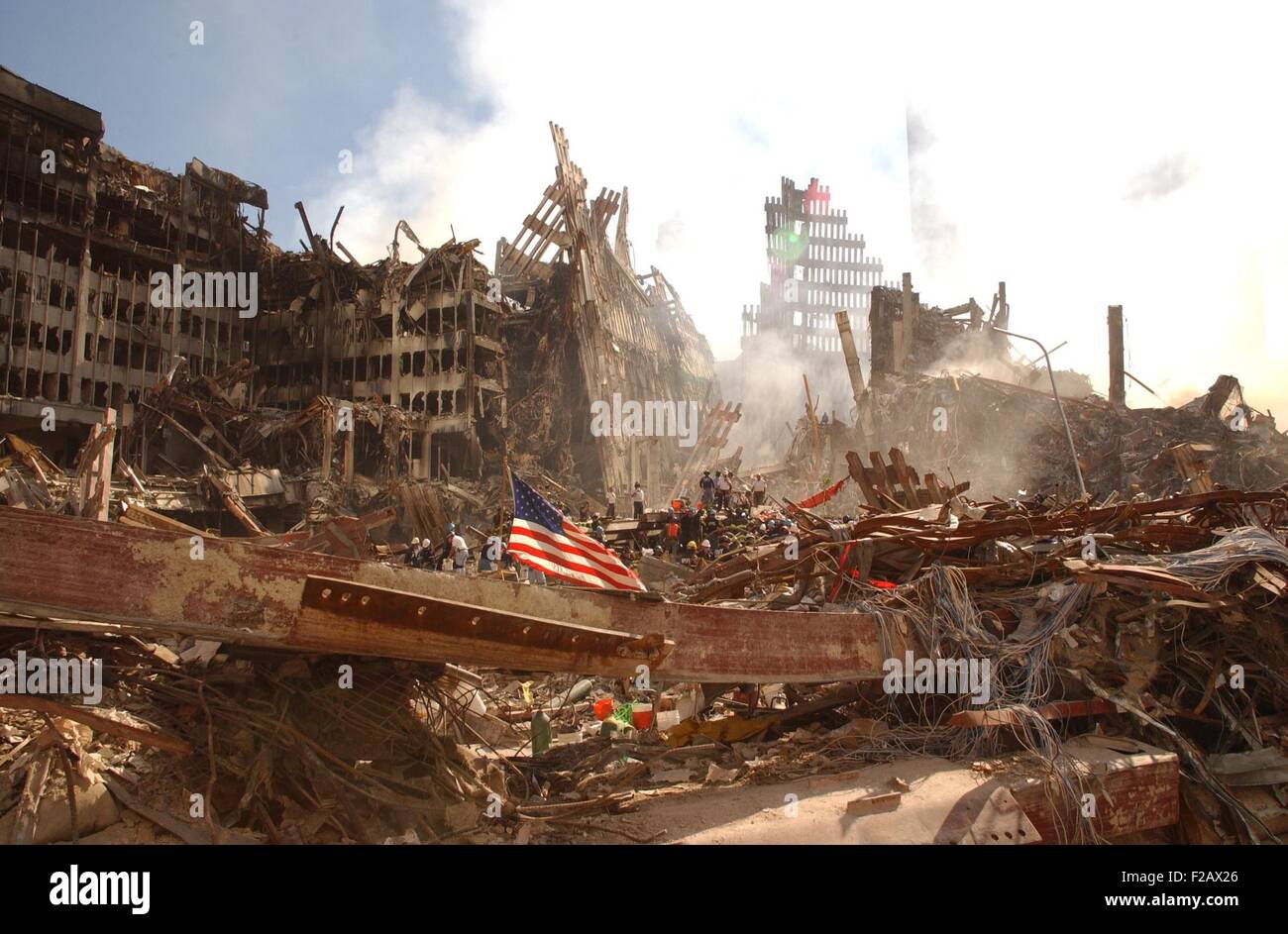 Smoke rises from the World Trade Center's collapsed North Tower. On the left are the remains of a lower structure, WTC 6. A large flag is secured to a beam in the foreground. New York City, Sept. 16, 2001. (BSLOC 2015 2 84) Stock Photo