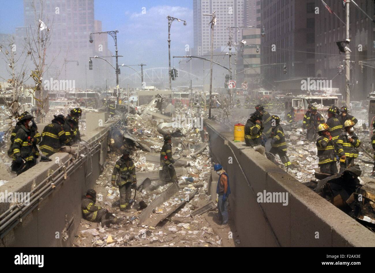 Fireman and other rescue workers on the northwest corner of the World Trade Center site. The view is to the north, up the West Side Highway (West Street) shortly after the collapse of both Twin Towers. Some men are seated, while others leaning and adjusting facemasks. Many vehicles were damaged by falling debris. (BSLOC_2015_2_57) Stock Photo