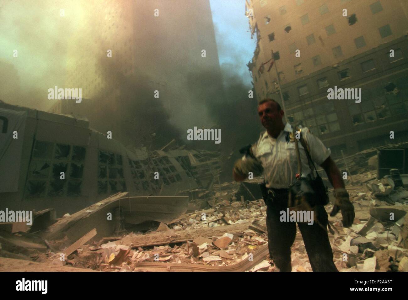 New York City policeman in ruins following September 11th terrorist attack on World Trade Center. He stands in the rubble with the north pedestrian bridge over West Side Highway (West St.). In the background left is World Financial Center 2 (WFC2) and at right, WFC3. (BSLOC 2015 2 50) Stock Photo